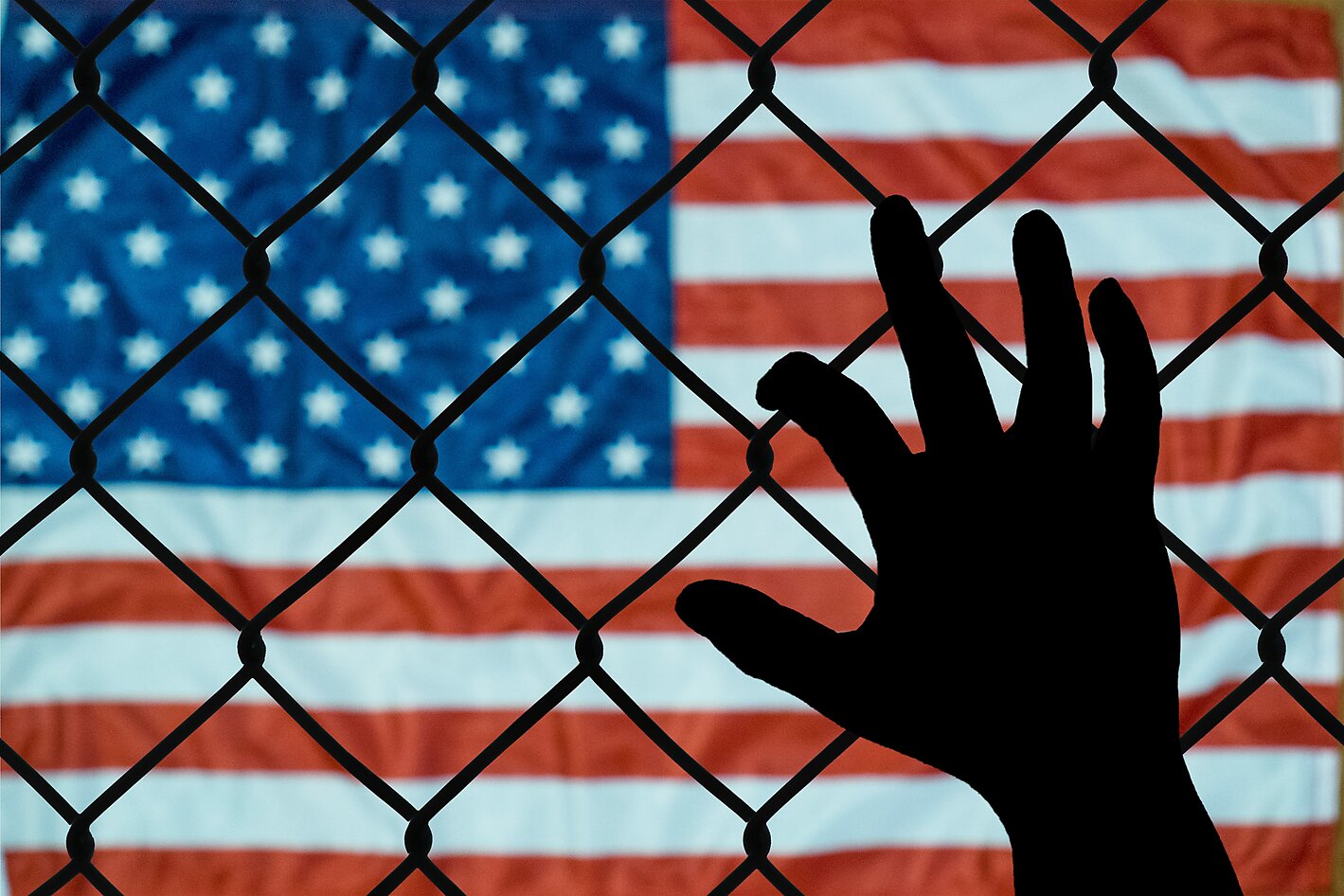 Hand holding a fence with American flag in the background