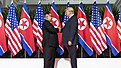 Kim Jong-un and Donald Trump shaking hands in front of US and North Korean flags