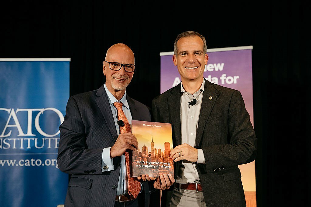 Michael Tanner and Eric Garcetti smiling and holding up a copy of "Cato's Project on Poverty and Inequality in California."